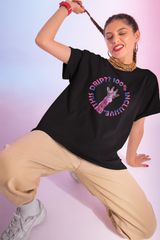 Bold streetwear statement tee from ANTI featuring a vibrant pink giraffe graphic with the slogan “100% Inclusive Drip??” in rainbow gradient typography, modeled by a confident individual embracing gender-fluid style on a pastel pink and blue background.