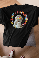 Black ANTI gender-neutral graphic t-shirt laid on a grey seat against a wooden floor, spotlighting a dramatic white marble statue with rainbow-tinted glasses and rainbow-hued lettering that reads “THIS DRIP?? 100% INCLUSIVE.” A bold, pride-centric fashion statement designed for queer-forward and expressive streetwear lovers.

