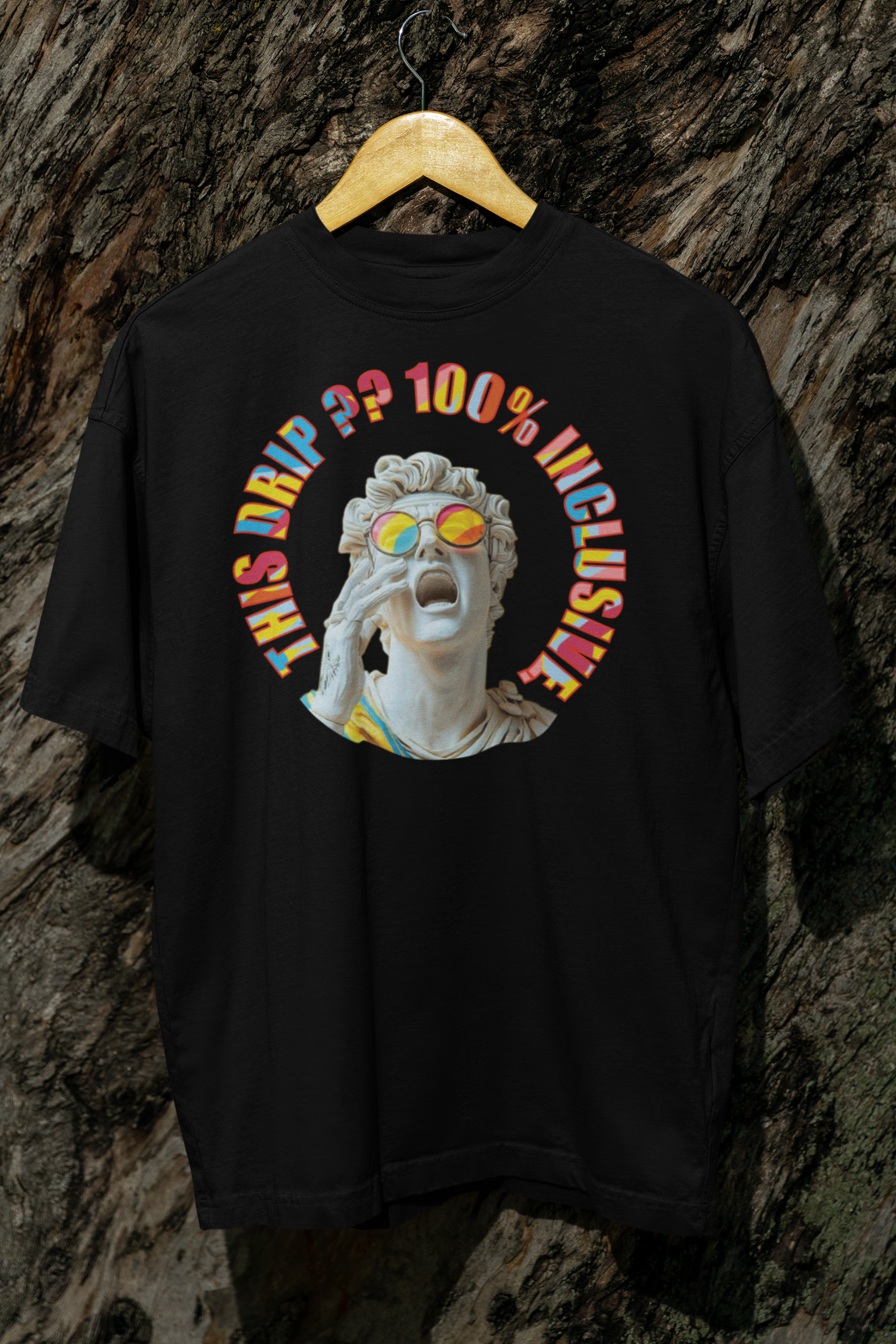 Black oversized t-shirt from ANTI hanging on a wooden hanger in front of a textured bark backdrop. Centered is a grayscale statue head wearing vivid rainbow sunglasses, surrounded by the phrase “THIS DRIP?? 100% INCLUSIVE” in bold multicolor typography. A rebellious, LGBTQIA+ inclusive fashion piece designed to defy norms.

