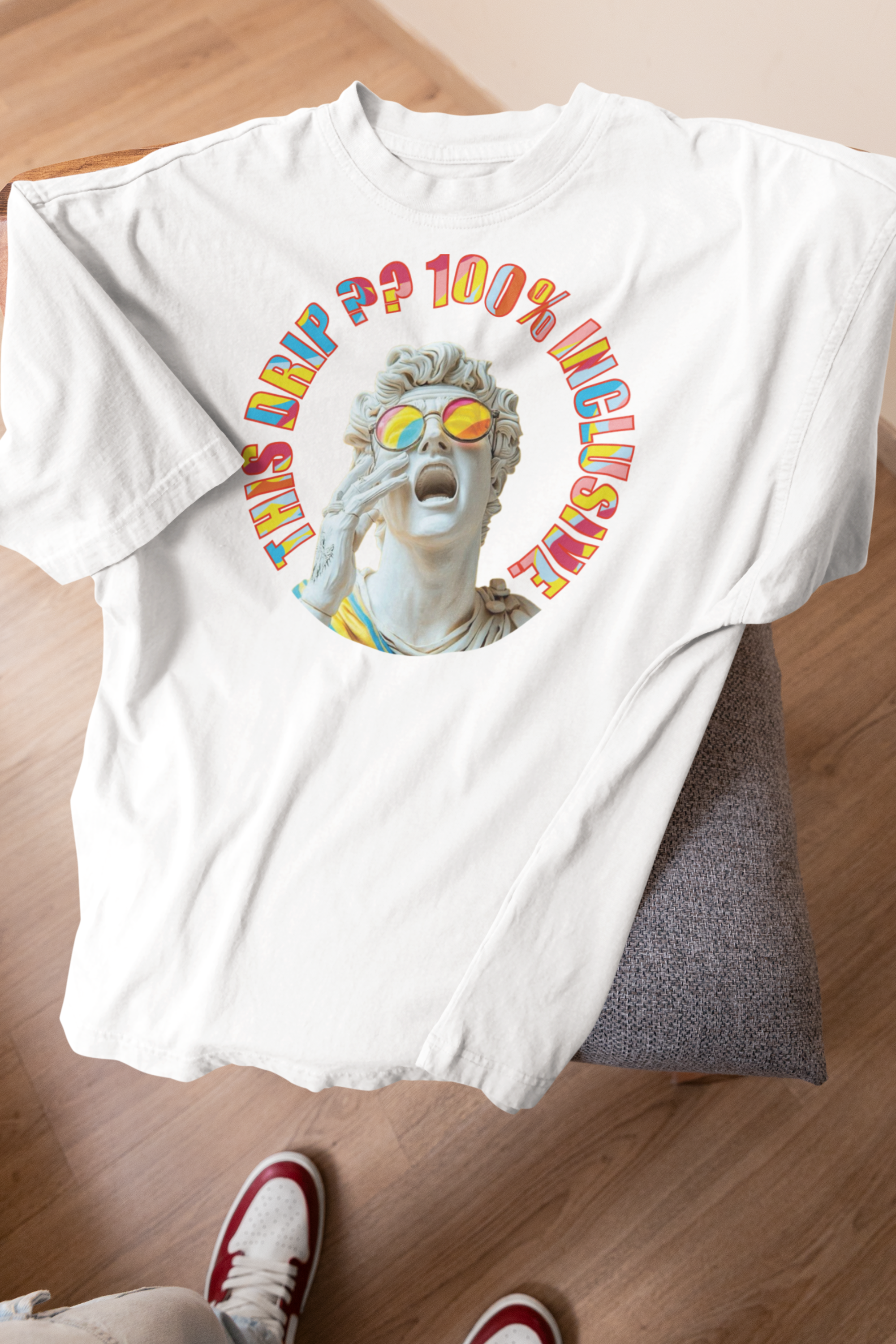 Laid-flat white t-shirt from ANTI on a wooden floor, with a Greco-Roman style statue screaming in rainbow sunglasses. Encircled by text “THIS DRIP?? 100% INCLUSIVE” in bold, multi-colored font. A unisex, queer-celebratory tee embodying inclusive style and anti-conformity pride fashion.

