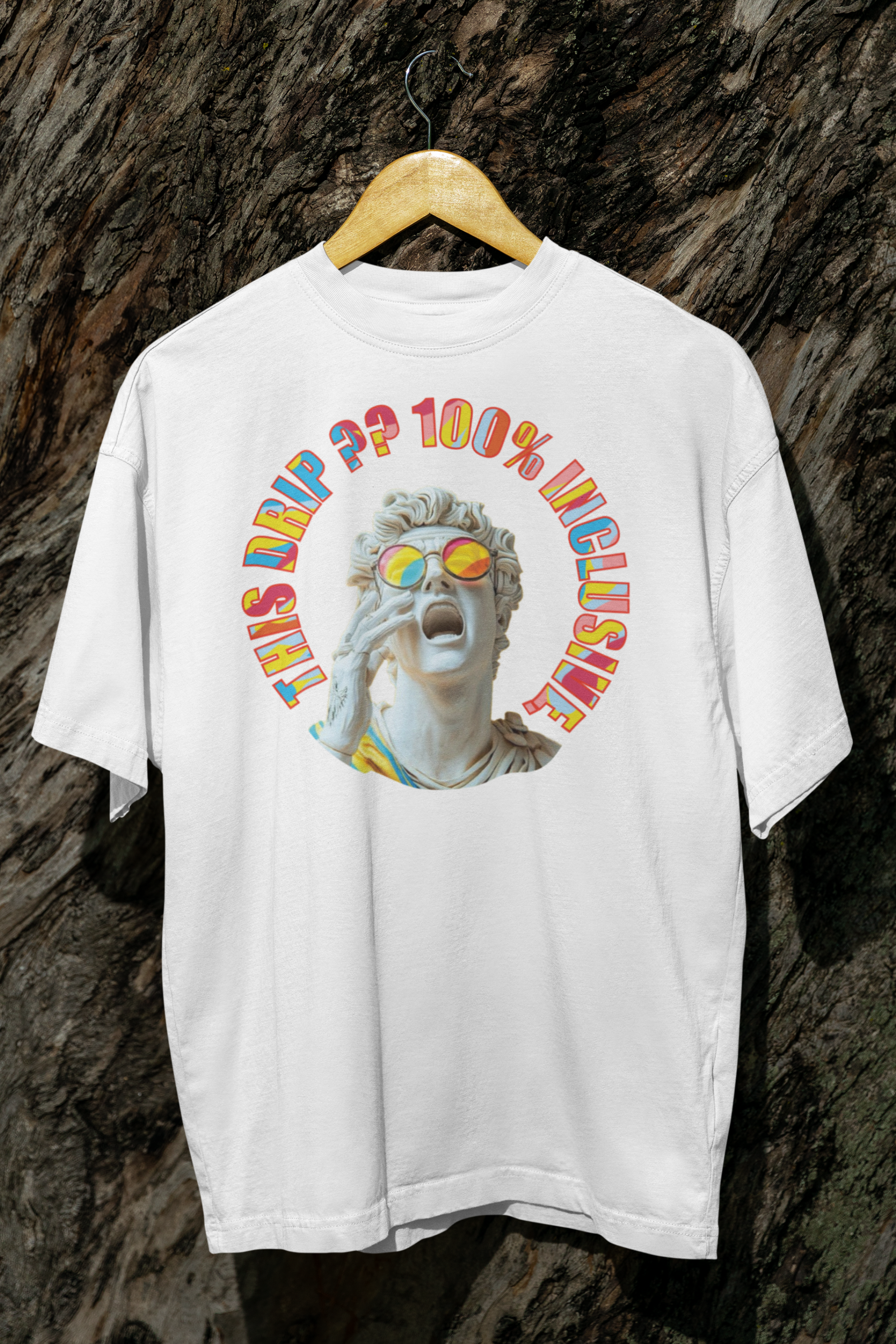A white unisex streetwear t-shirt from ANTI hanging against a rugged tree background, featuring a 3D-style Greco-Roman statue head with rainbow sunglasses and hand to mouth in a yell. The vibrant retro text around the statue reads “THIS DRIP?? 100% INCLUSIVE,” symbolizing LGBTQIA+ pride and inclusive fashion.

