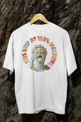 A white unisex streetwear t-shirt from ANTI hanging against a rugged tree background, featuring a 3D-style Greco-Roman statue head with rainbow sunglasses and hand to mouth in a yell. The vibrant retro text around the statue reads “THIS DRIP?? 100% INCLUSIVE,” symbolizing LGBTQIA+ pride and inclusive fashion.

