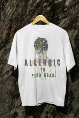 White oversized T-shirt reading "Allergic to Dickhead," styled outdoors; inclusive, gender-neutral streetwear top.