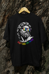 “ANTI’s black ‘Don’t Hide the Pride’ T-shirt hanging on a wooden hanger against a tree, showcasing a queer-positive design of a Greco-Roman face with rainbow sunglasses and bold rainbow typography—perfect for inclusive pride fashion.”

