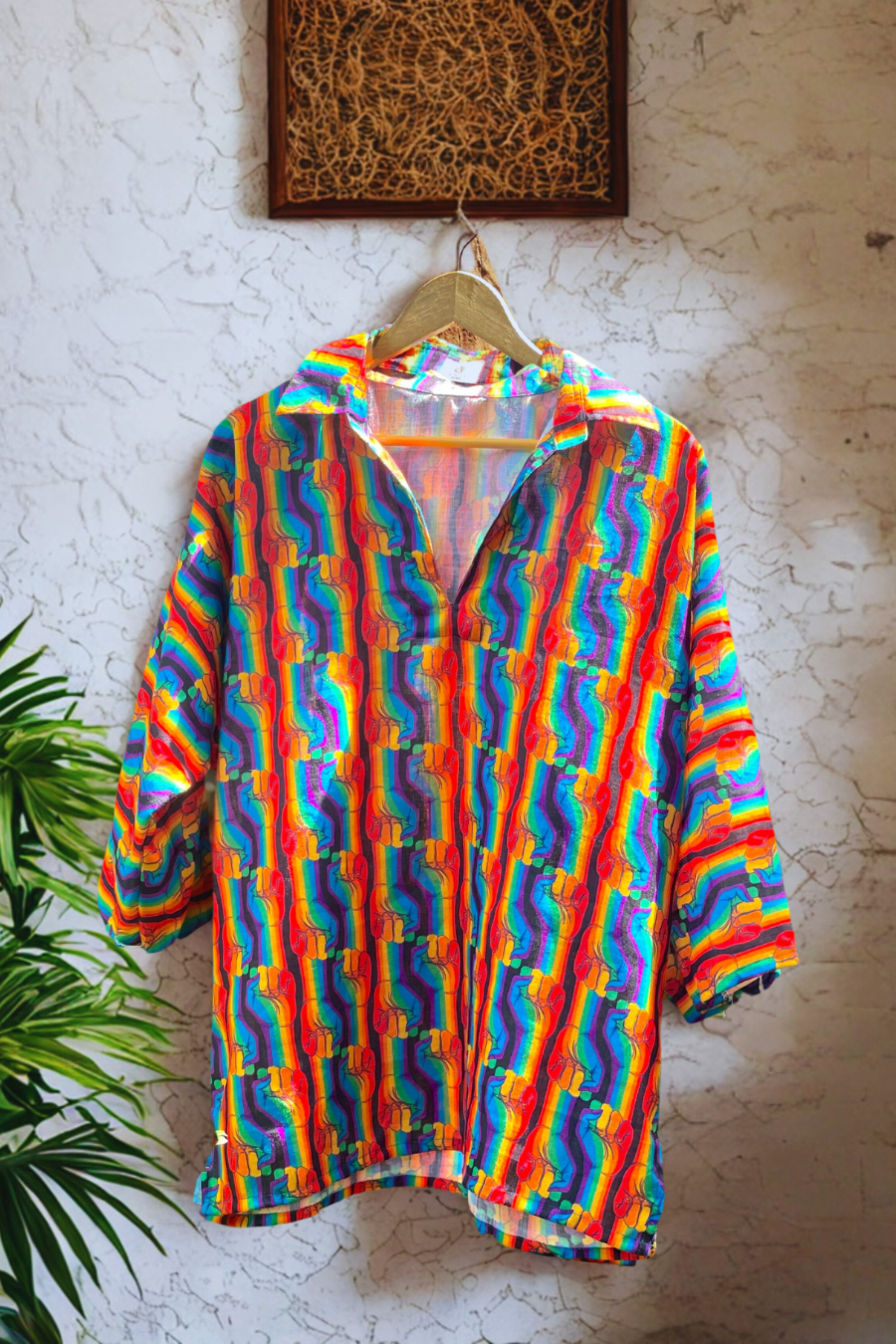 Front-facing view of ANTI Fist Forward rainbow shirt with raised fist prints in vertical stripes, buttonless V-neck design, and flowing silhouette, symbolizing queer resistance and pride.