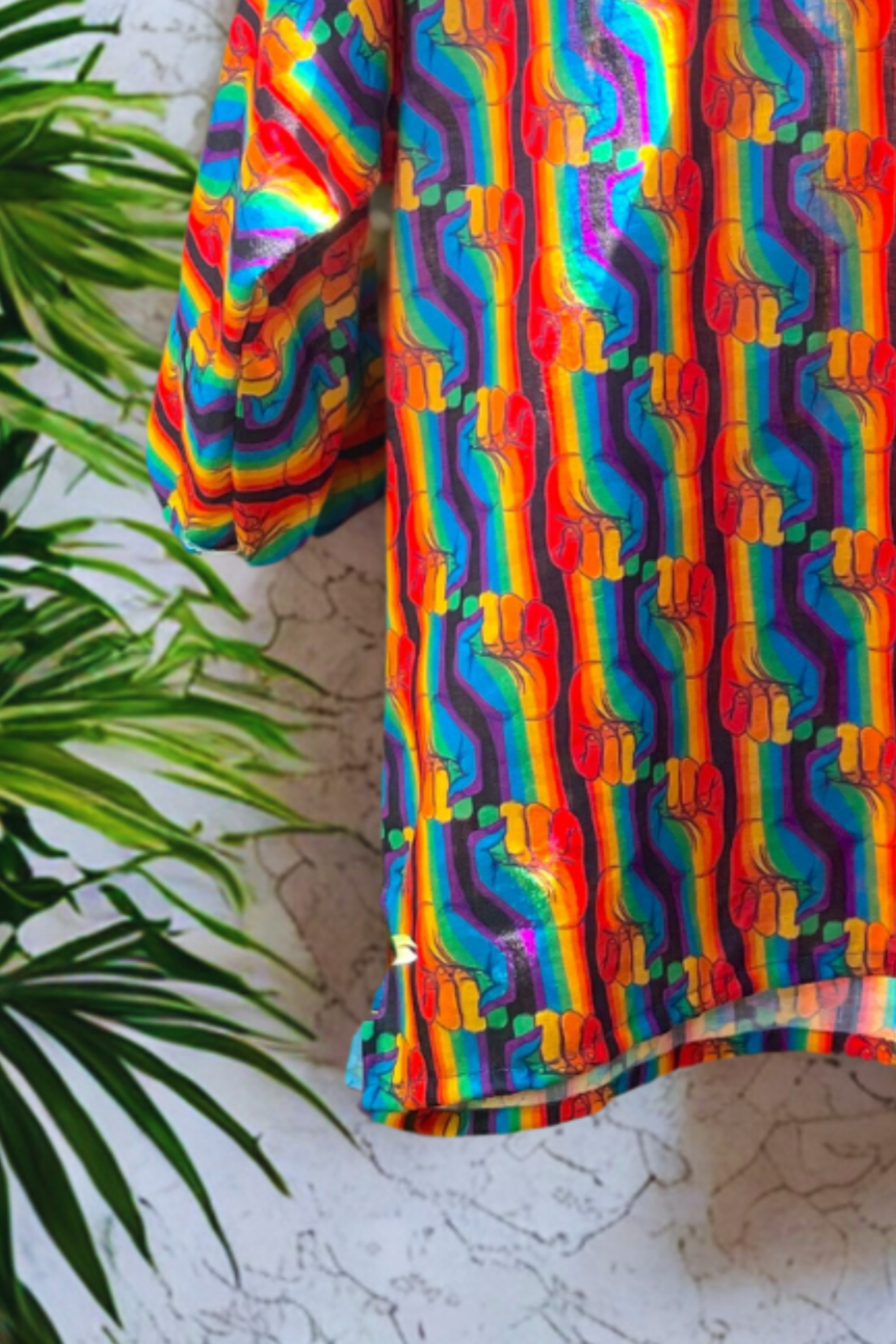 Longline ANTI Fluid Unity shirt with vibrant rainbow fist design extending to mid-thigh, relaxed drop shoulder cut, and buttonless front, displayed on hanger to highlight drape and inclusivity.