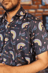 Close-up of a black short-sleeved shirt from ANTI, showcasing its detailed print of pastel rainbow arcs and handwritten-style 'love is love' text. The fabric appears soft and flowing, highlighting the inclusive and expressive design for LGBTQIA+ affirming fashion.