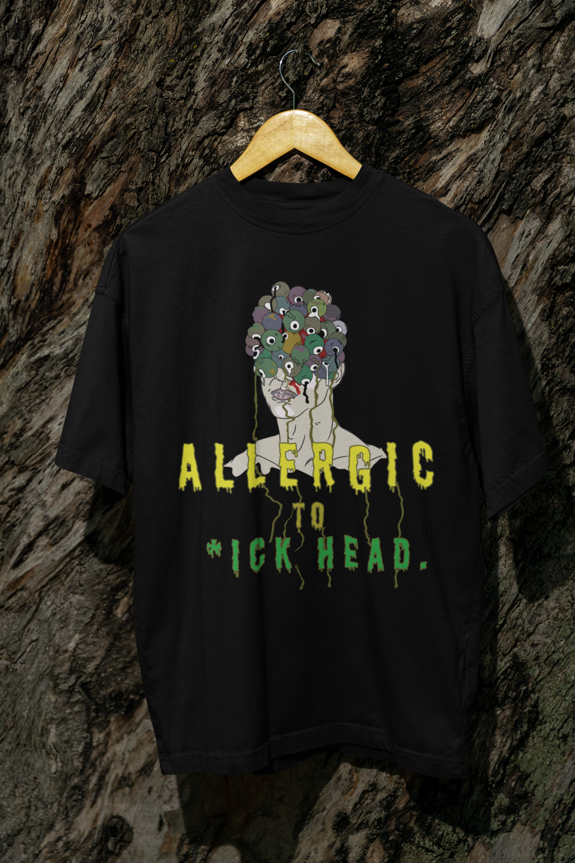 Black oversized T-shirt with "Allergic to Dickhead" text, hanging on tree; gender-fluid, inclusive streetwear tee.