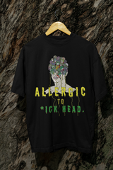 Black oversized T-shirt with "Allergic to Dickhead" text, hanging on tree; gender-fluid, inclusive streetwear tee.