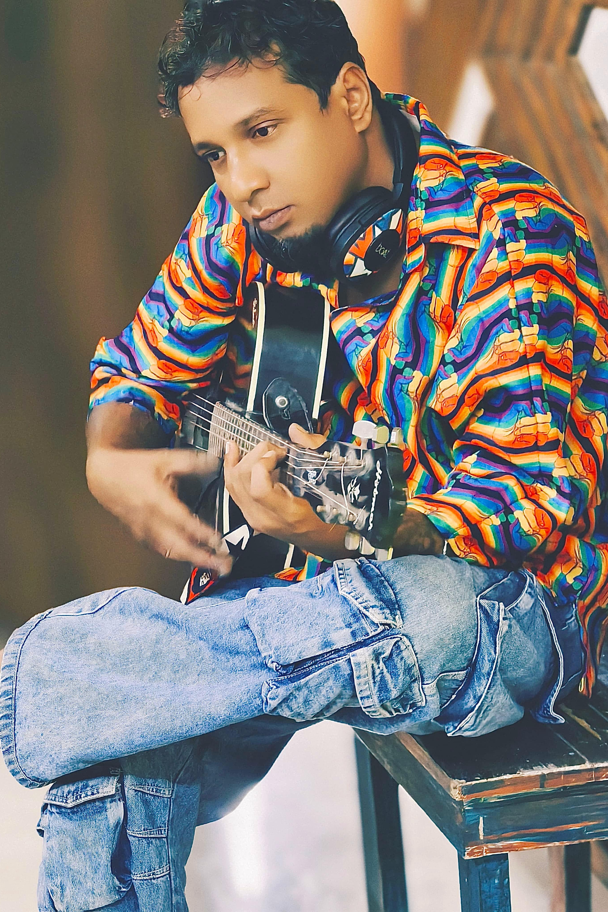 Model wearing ANTI Noise of Freedom rainbow shirt with fist prints, casually styled with cargo jeans and guitar, radiating bold queer joy and rebellious energy in a music studio setting.