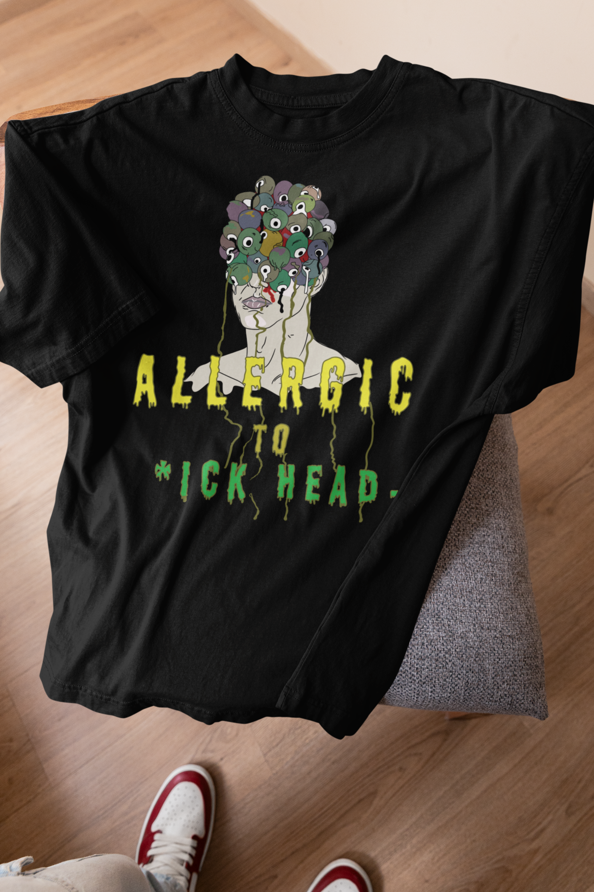 Black oversized T-shirt on a stool with bold “Allergic to Dickhead” print; rebellious queer-inclusive fashion.