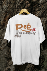 White gender-inclusive t-shirt hanging in front of a rugged wood backdrop, with a bold graffiti-style design reading “Peg the Patriarchy” in orange, red, and grey; the letter 'P' features a worn texture resembling a cigarette butt, symbolizing subversive anti-patriarchal sentiment.

