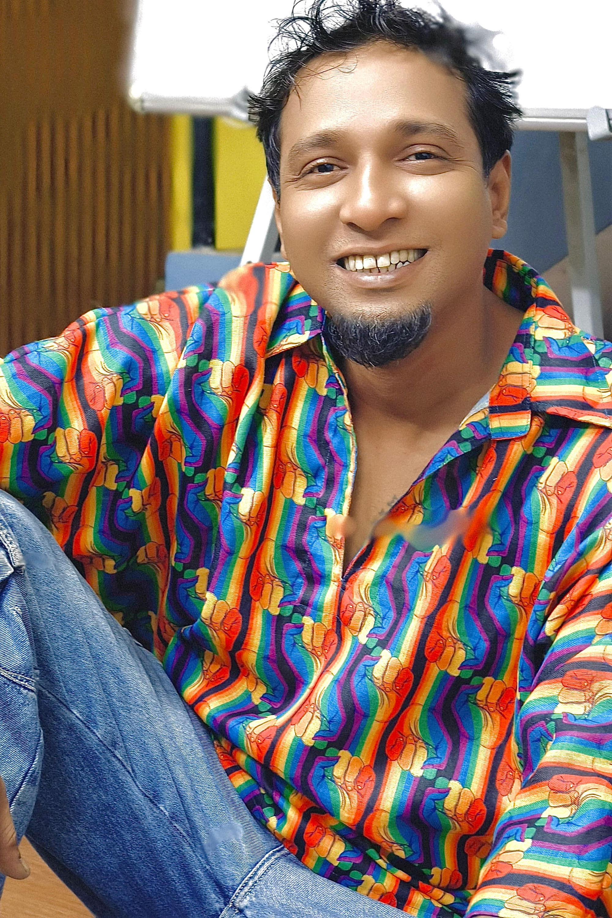 Model in ANTI Pride Pulse rainbow fist shirt smiling confidently in urban setting; styled effortlessly to represent non-binary expression and vibrant queer fashion.