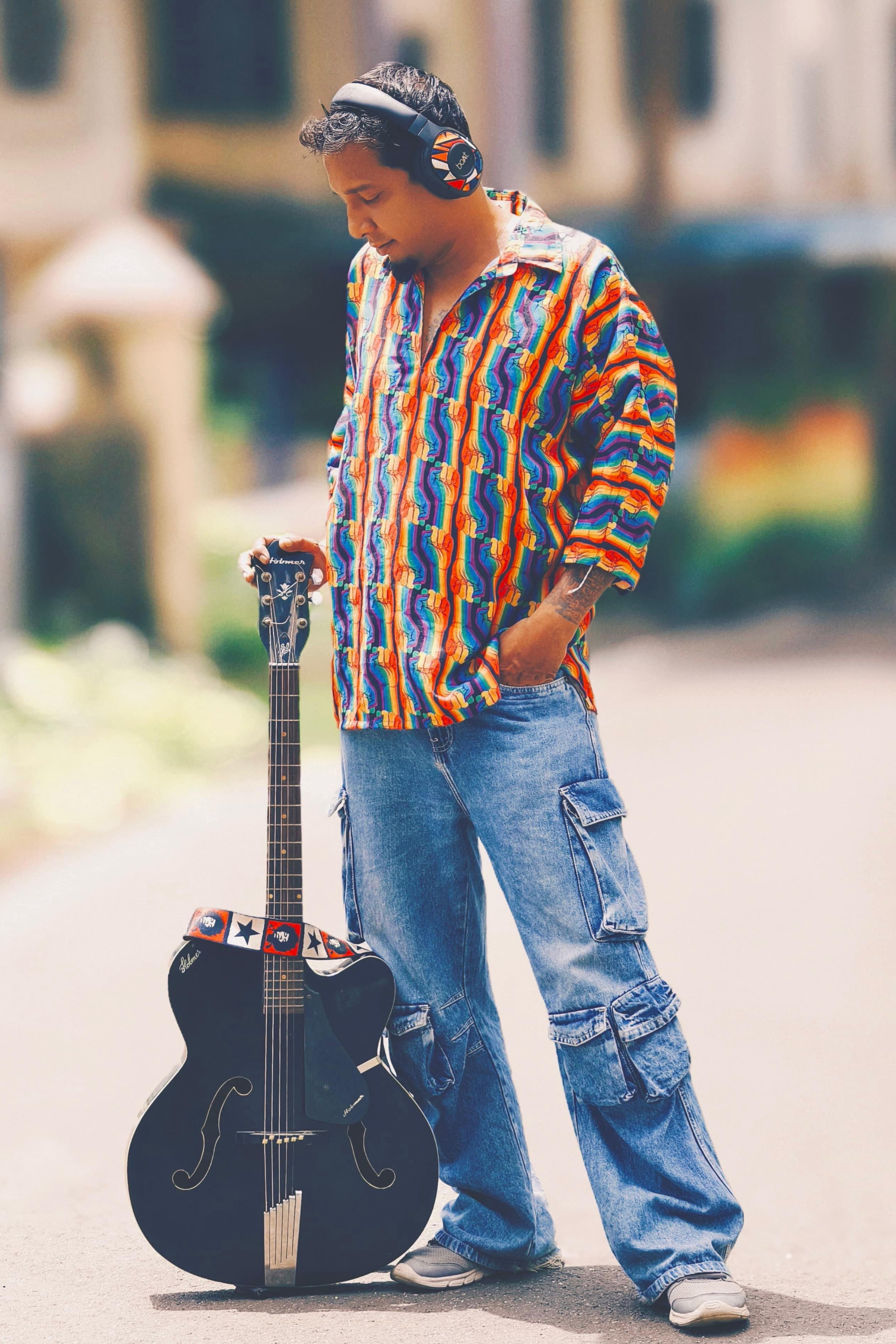 Queer artist wearing ANTI Rebel Raga rainbow shirt while playing guitar; captured in raw, emotive lighting that highlights the shirt’s inclusive message and sound-driven style ethos.