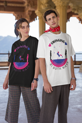 Gender-fluid model wearing a bold black ANTI t-shirt featuring a playful swing graphic with bi pride colors and the inclusive slogan “Swinging Bi Both Ways,” styled with checkered wide-leg pants and subtle accessories in a sunlit heritage setting.


