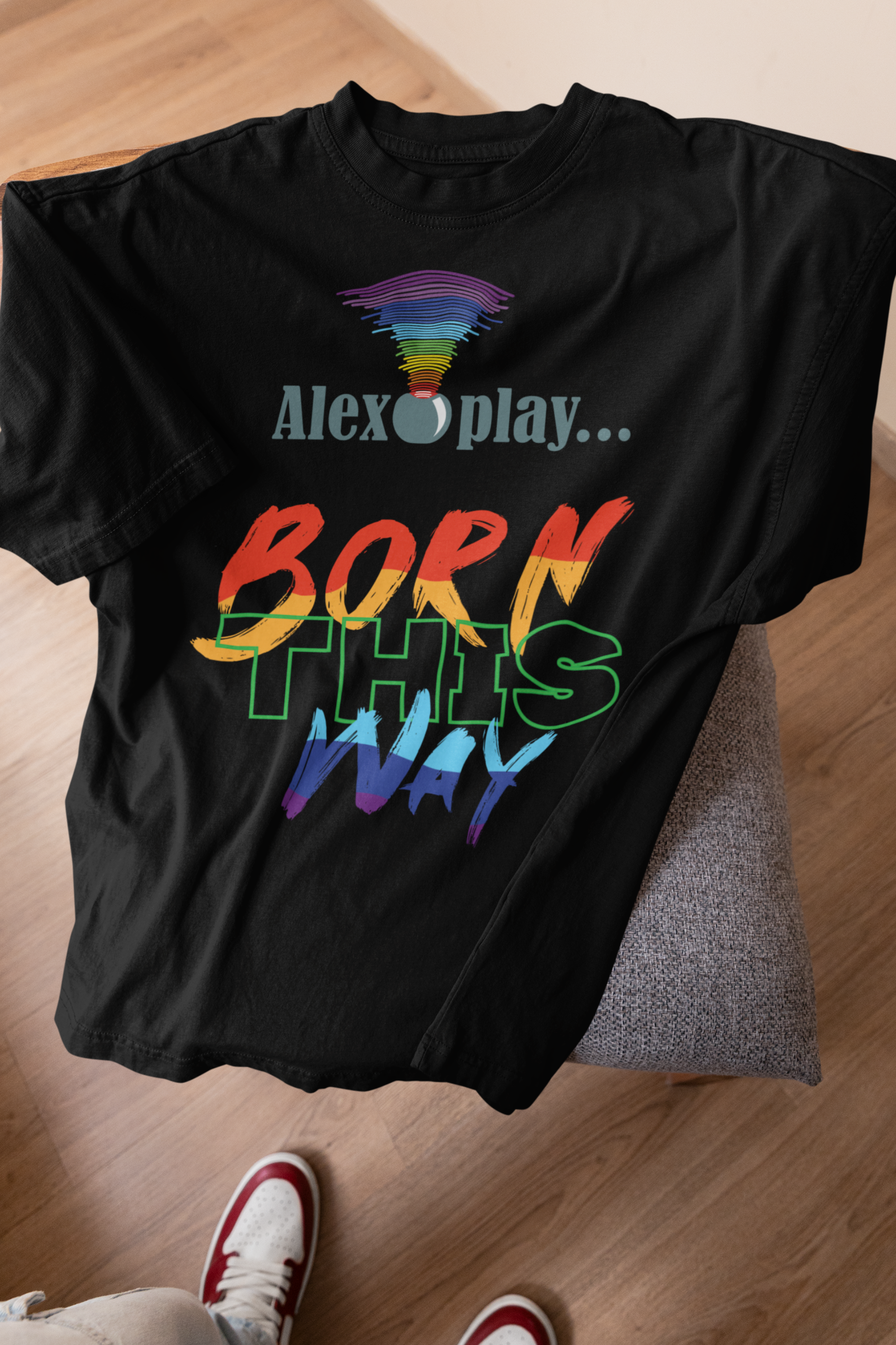 Black “Alexa, Play Born This Way” T-shirt, with bold text centered on the chest. The photo emphasizes the t-shirt’s soft texture and relaxed structure, appealing to LGBTQIA+ individuals seeking comfortable, empowering fashion. 