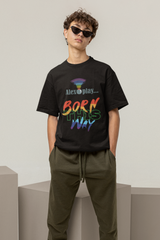 Model stands confidently in front of a neutral backdrop wearing the "Alexa, Play Born This Way" graphic T-shirt, styled in black with bold white typography across the chest. The shirt has a relaxed, oversized fit, symbolizing freedom of expression and body positivity. The model’s stance, with hands in pockets and gaze forward, exudes self-assurance and unapologetic queer pride. This look represents modern LGBTQ+ inclusive fashion with a streetwear edge.