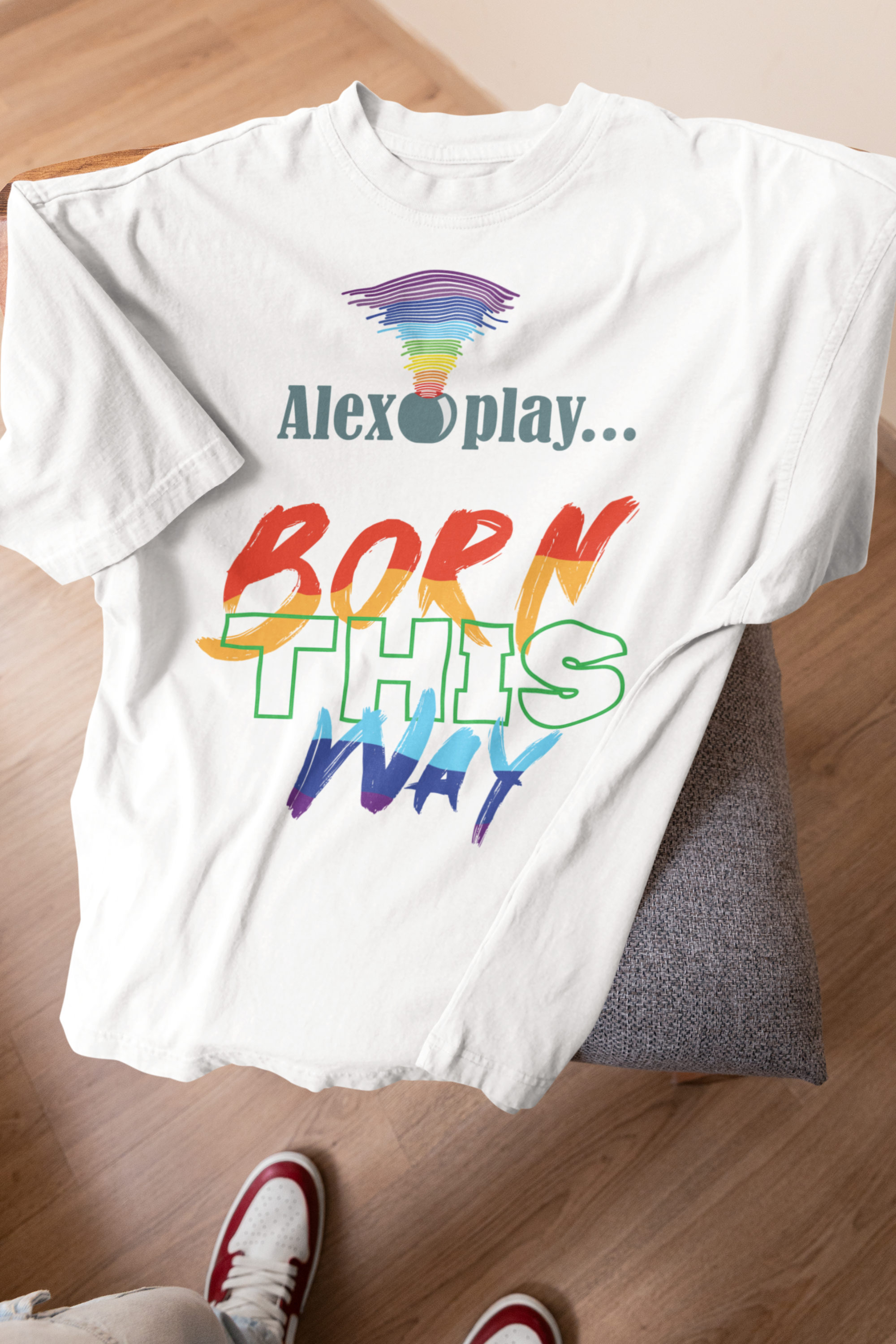 Flat-lay close-up of the “Alexa, Play Born This Way” T-shirt design. Bold, uppercase white typography spans the chest of the black fabric, making the queer cultural reference instantly recognizable. The crisp lettering and contrast are showcased for detailed product viewing — perfect for emphasizing the statement-making quality of this gender-inclusive tee.