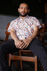 Man sitting on a wooden chair wearing a colorful patterned shirt.