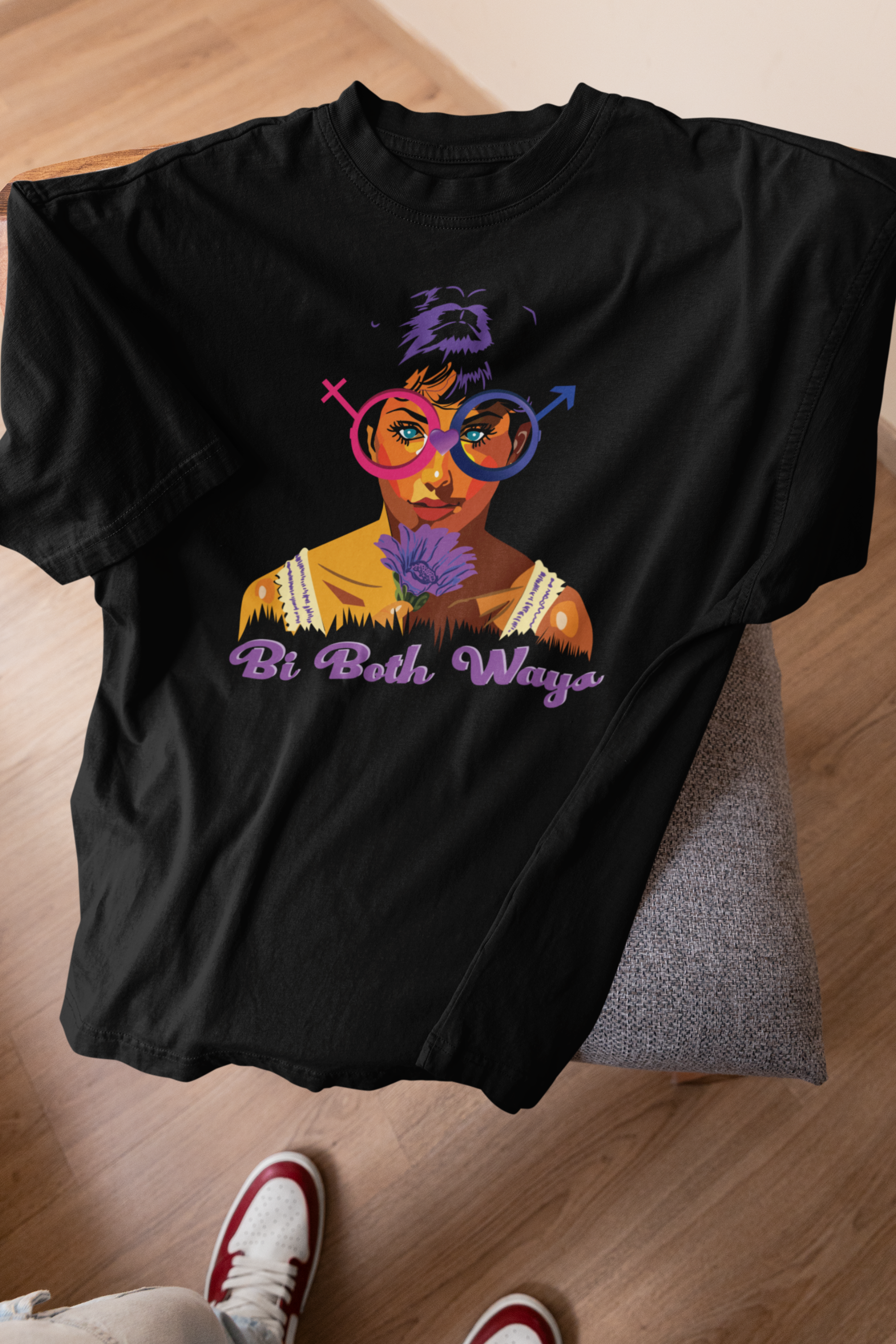 Black Bi Both Ways oversized t-shirt draped over a wooden stool with a bold bi pride graphic, shot in soft natural light.

