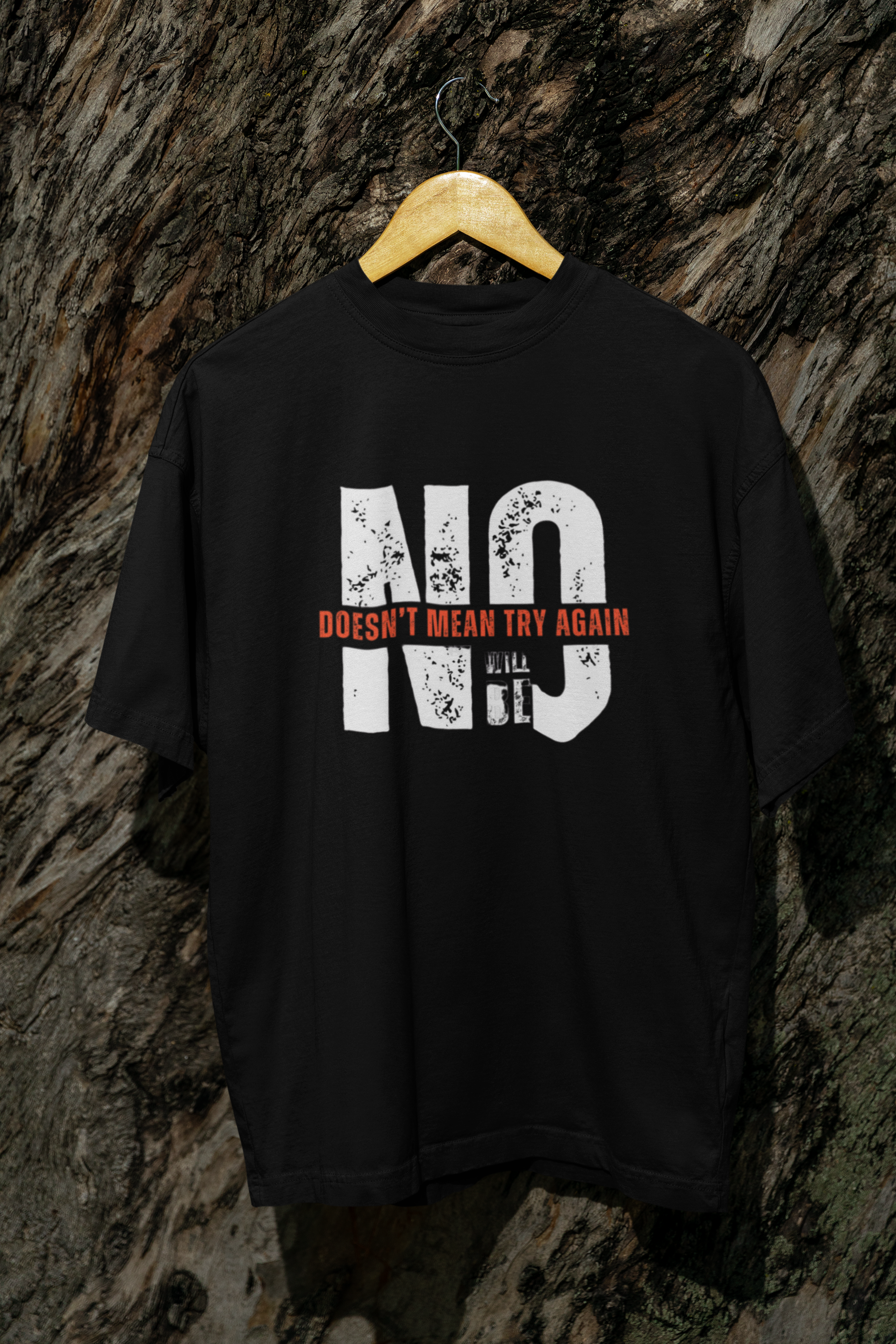 Black oversized t-shirt with bold consent slogan, unisex streetwear style, displayed outdoors on tree for edgy vibe
