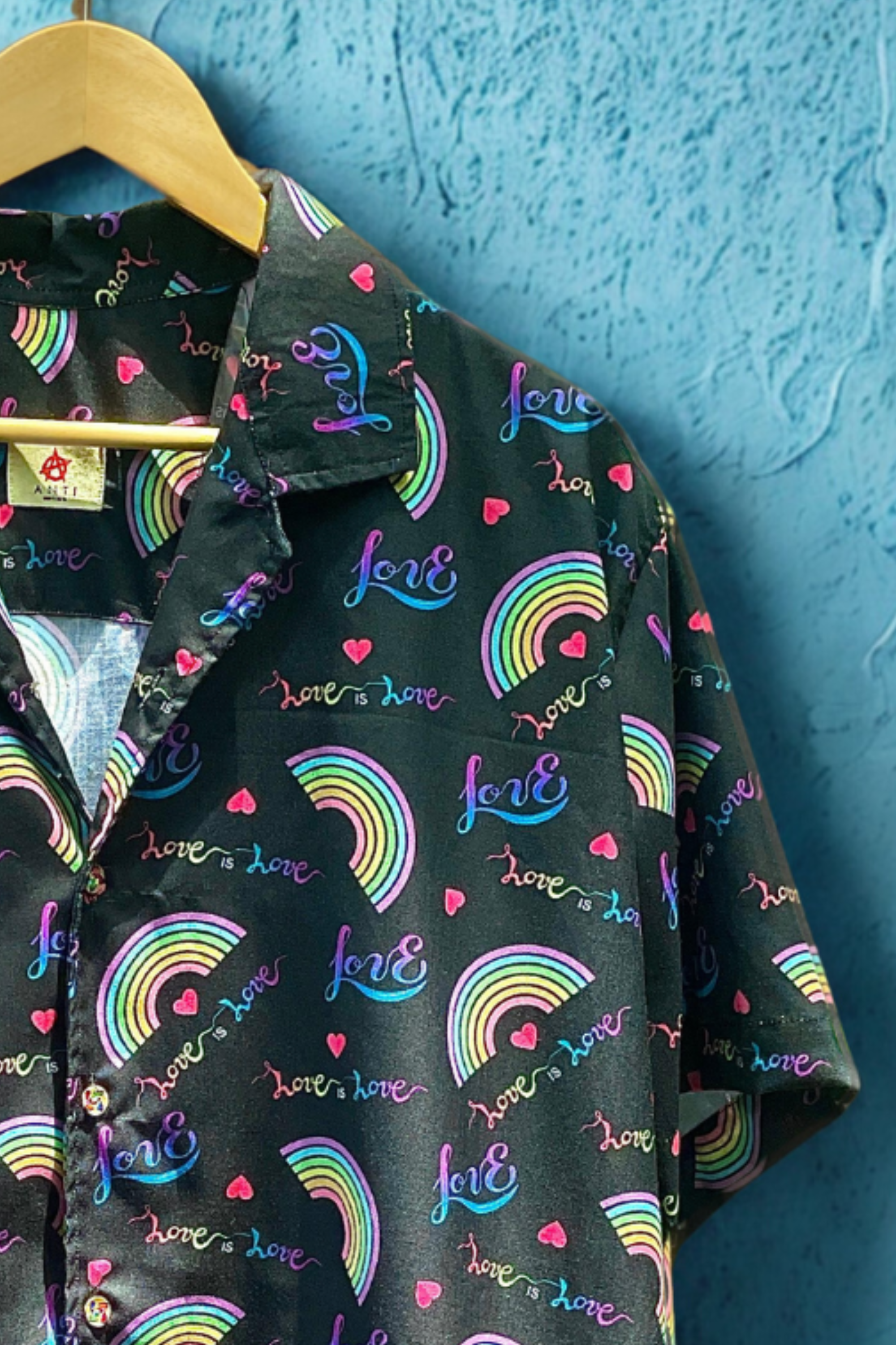Side angle of ANTI’s rainbow satin button-up Pride shirt showing glossy fabric, vibrant all-over print with “love is love” typography, and a gender-expansive fit perfect for queer and trans fashion expressions.