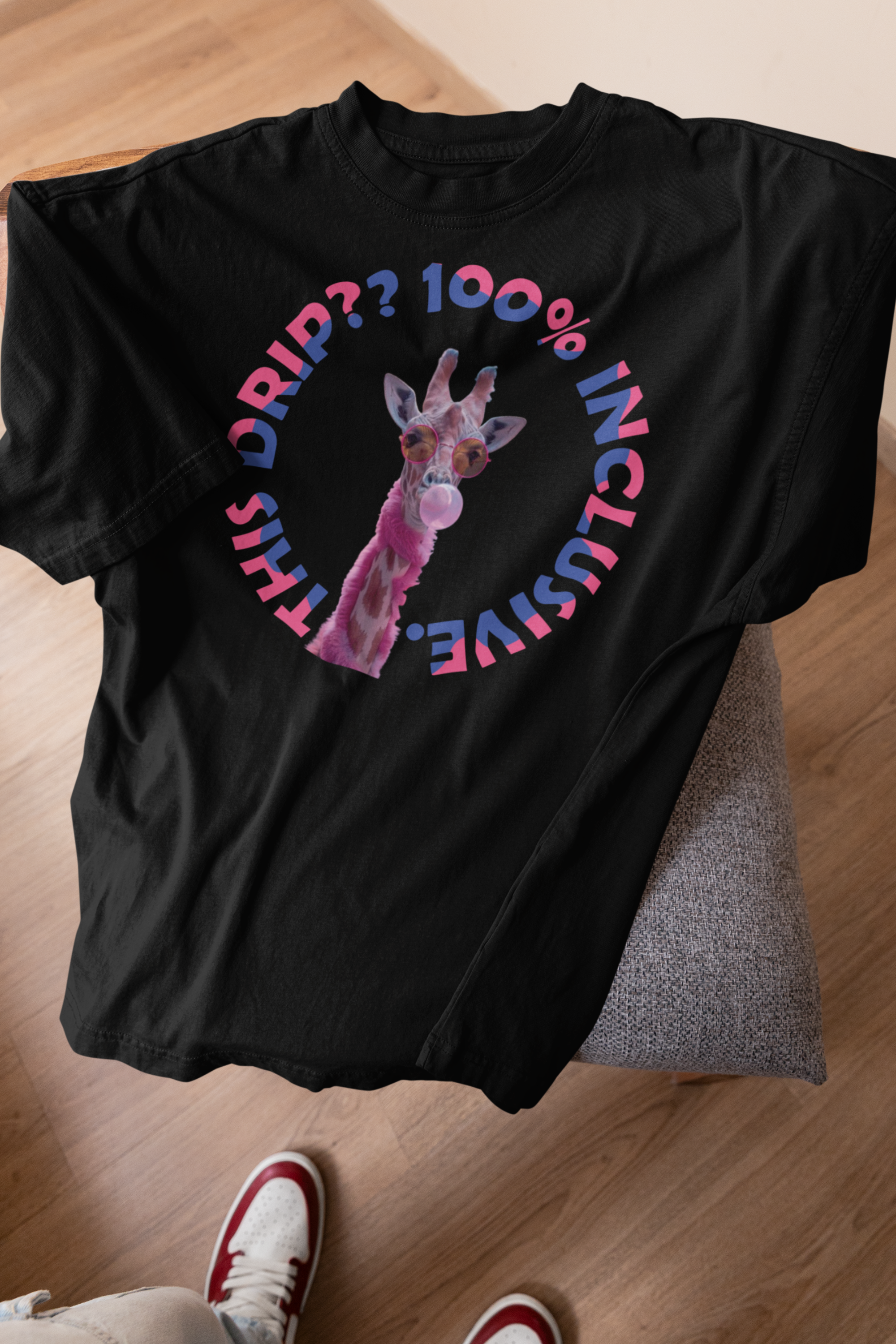 Flat lay of a black unisex streetwear T-shirt featuring a vibrant print of a pink giraffe blowing bubble gum, wearing sunglasses, surrounded by the bold text “THIS DRIP?? 100% INCLUSIVE” in a bisexual pride color palette of blue, purple, and pink — a bold gender-neutral statement tee by ANTI celebrating LGBTQIA+ identity and radical inclusion.