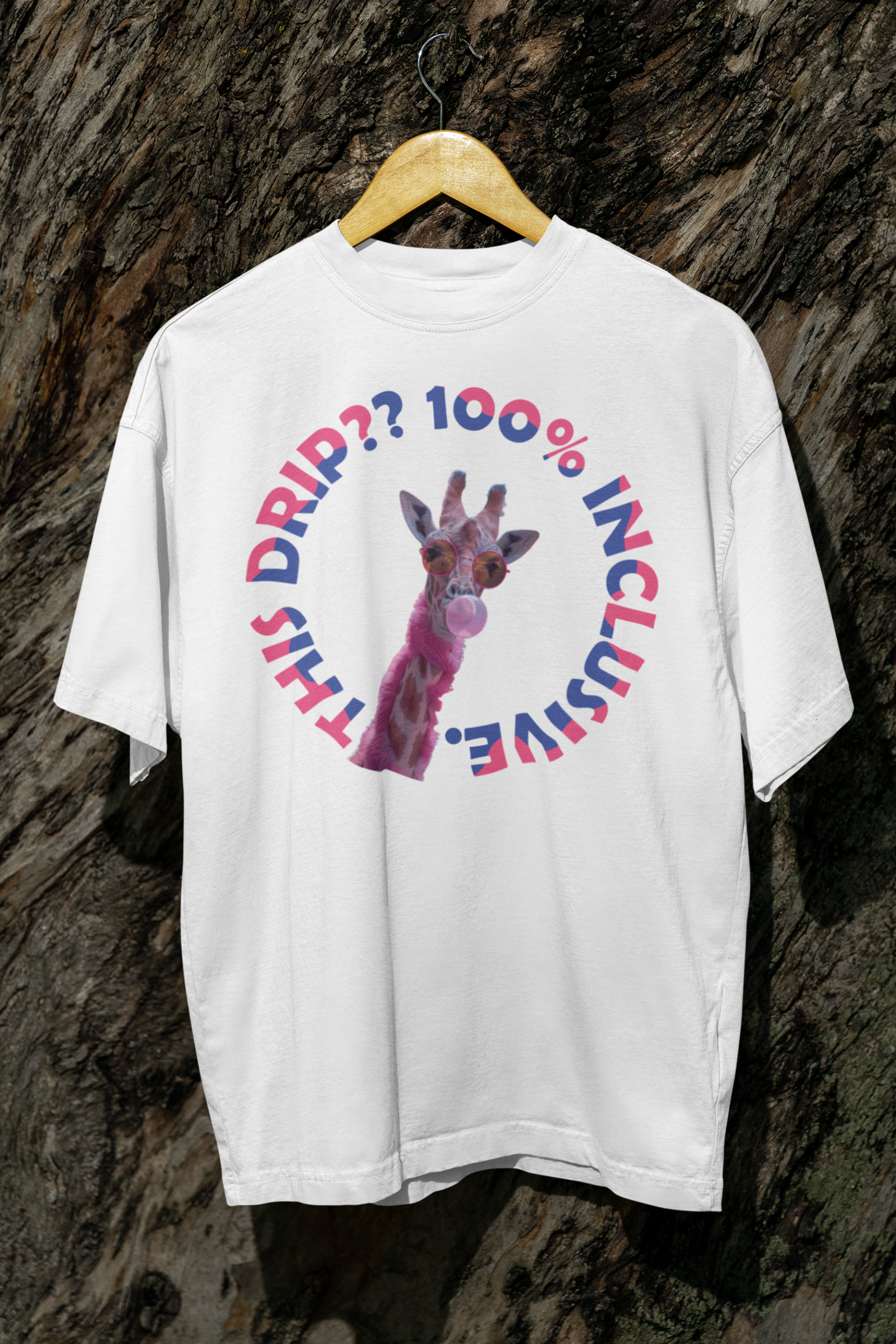 White oversized T-shirt hanging outdoors against a tree trunk, showcasing a quirky, fashion-forward design of a pink giraffe with sunglasses and bubblegum, framed by the phrase “THIS DRIP?? 100% INCLUSIVE” in bisexual flag colors — a gender-fluid, LGBTQIA+-affirming fashion piece from ANTI’s unapologetic inclusive apparel collection.