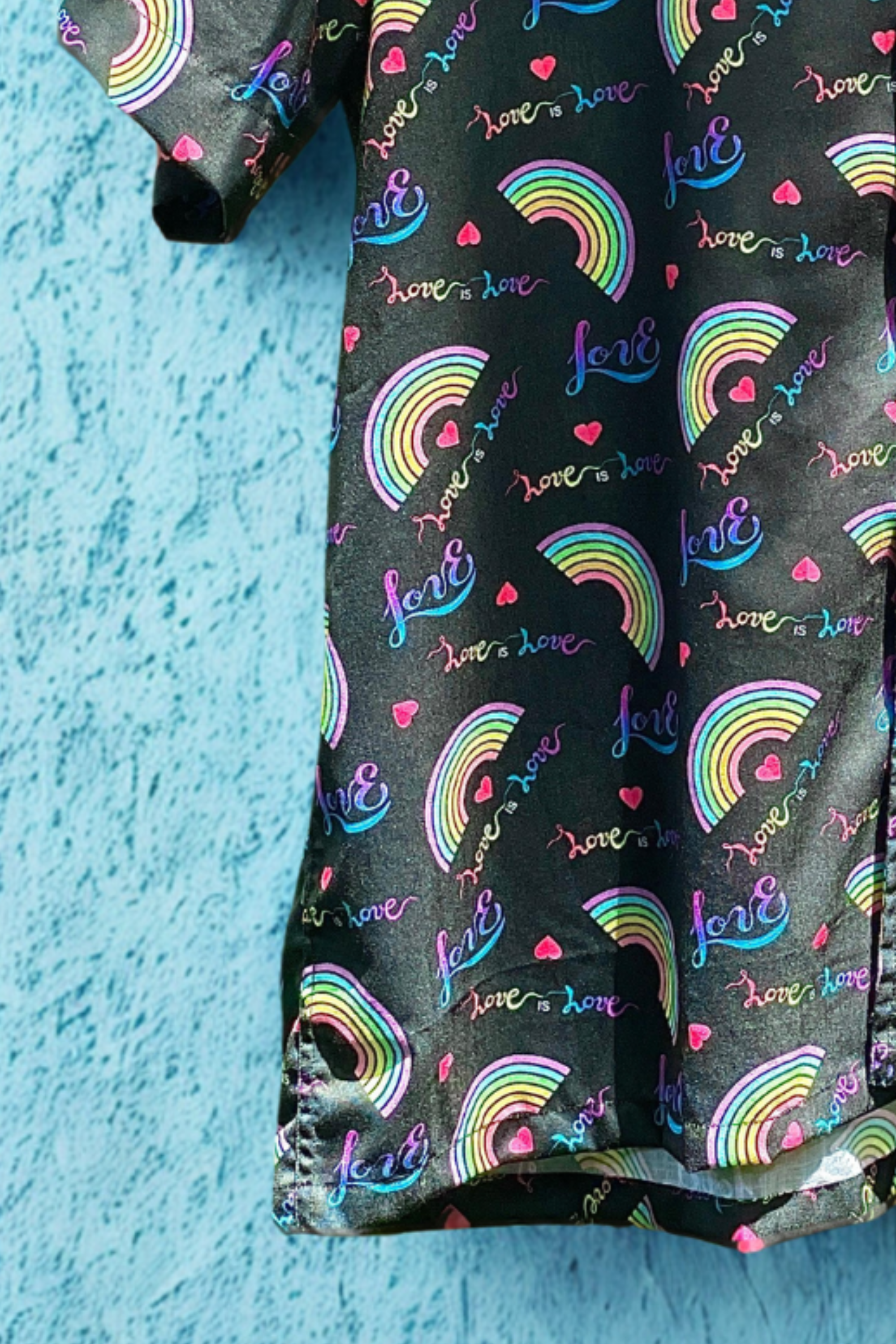 Detailed zoom-in of ANTI’s “Love is Love” button-up shirt showcasing luxe cotton fabric, rainbow heart patterns, and affirming LGBTQIA+ messaging—capturing the intersection of fashion and identity.