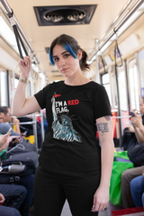  Person with blue highlights and a strong gaze wears a black inclusive graphic t-shirt with the Statue of Liberty raising a red flag and the phrase “I’M A RED FLAG”; urban subway background highlights ANTI’s genderless, rebellious pride apparel.

