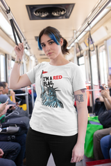 Confident person with blue hair and septum piercing wearing a white gender-fluid t-shirt featuring the Statue of Liberty holding a red flag with bold text saying “I’M A RED FLAG”; photographed on a public transit train, representing ANTI’s unapologetically queer streetwear fashion.