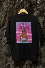 Black unisex t-shirt hanging outdoors against a textured tree bark, showcasing a powerful graphic of a trans person in a trans pride binder surrounded by celestial sparkles and a pink cloudy sky, with the statement “I’M IN TRANS” in bold, stylized font.
