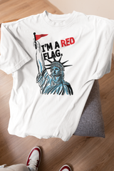 Flat-lay of ANTI’s "I’m a Red Flag" white graphic t-shirt draped over a chair, featuring a bold illustration of the Statue of Liberty raising a red protest flag with the statement “I’M A RED FLAG” in distressed typography—symbolizing rebellion, self-expression, and unapologetic identity in queer and inclusive fashion.

