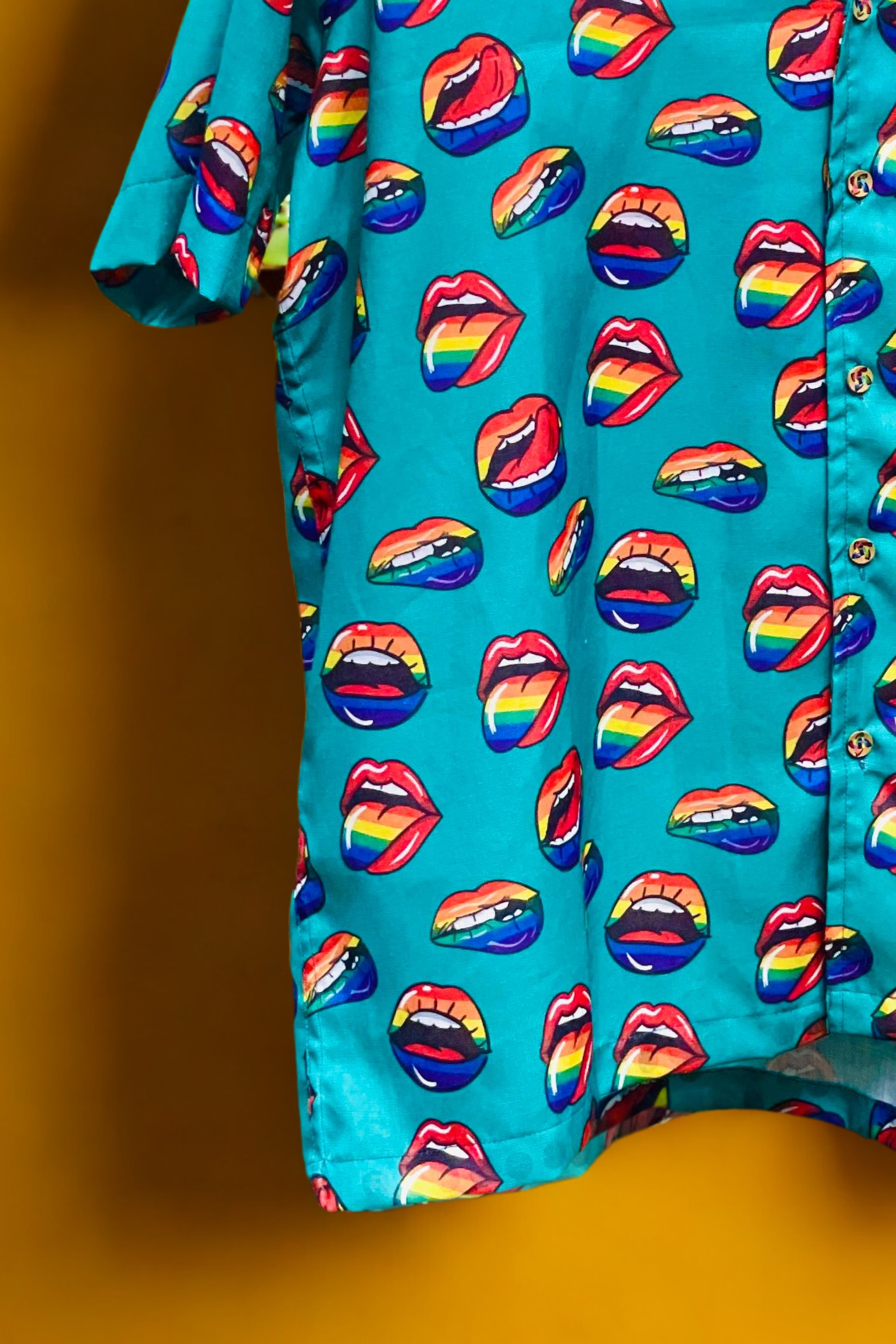 Flat-lay of a short-sleeve button-up shirt by ANTI with an all-over pattern of pink and red lips with open mouths on a pastel blue background. The graphic design fuses camp, queerness, and Y2K pop art aesthetics into a bold, statement piece. With a relaxed fit and all-gender appeal, this shirt celebrates queer freedom, making it ideal for Pride events, festival fashion, or everyday empowerment.