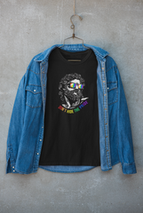 Black “Don’t Hide The Pride” t-shirt hung on a hanger beneath an open denim jacket against a concrete wall, showcasing a powerful rainbow-glasses sculpture design — styled for layered gender-neutral pride fashion by ANTI.