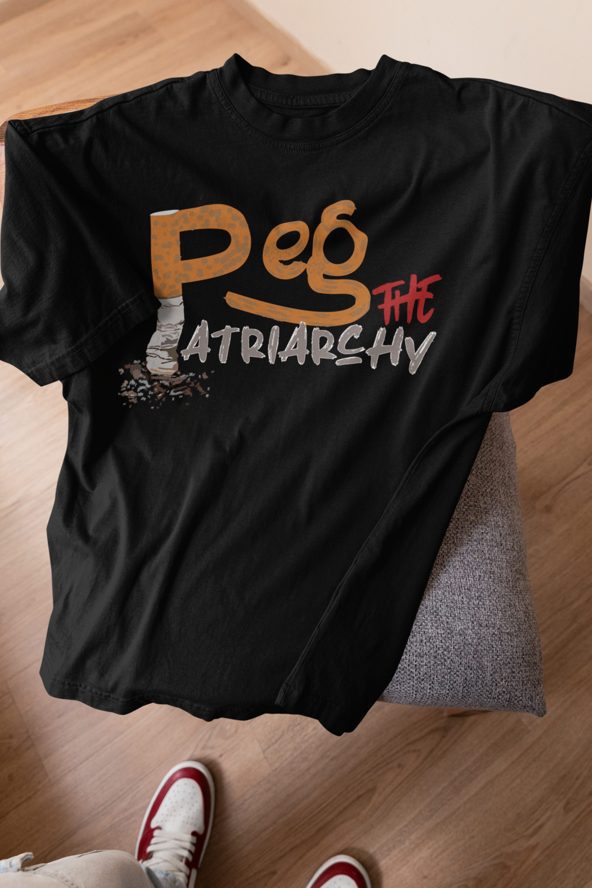 Black oversized unisex t-shirt draped over a wooden stool, featuring bold white “Peg the Patriarchy” print. A gender-fluid fashion essential from ANTI’s queer streetwear line, made for loud statements and all body types.