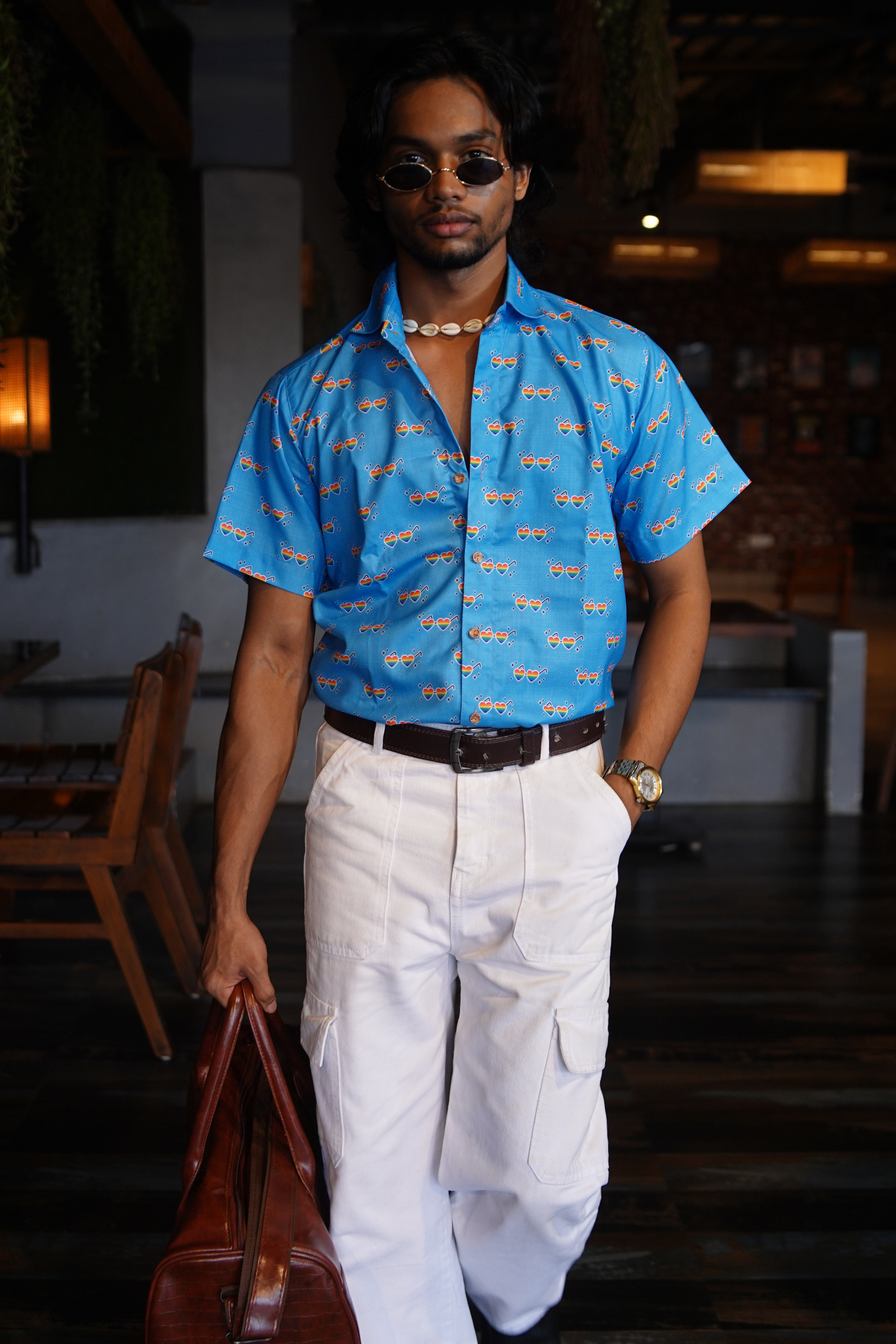 Man wearing a blue patterned shirt and white pants in an indoor setting
