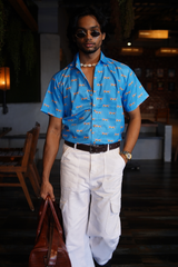 Man wearing a blue patterned shirt and white pants in an indoor setting