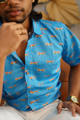 Close-up view of a blue button-down shirt with rainbow heart sunglasses and music notes, capturing the shirt’s detailed LGBTQIA+ inspired print and ANTI’s bold visual identity.