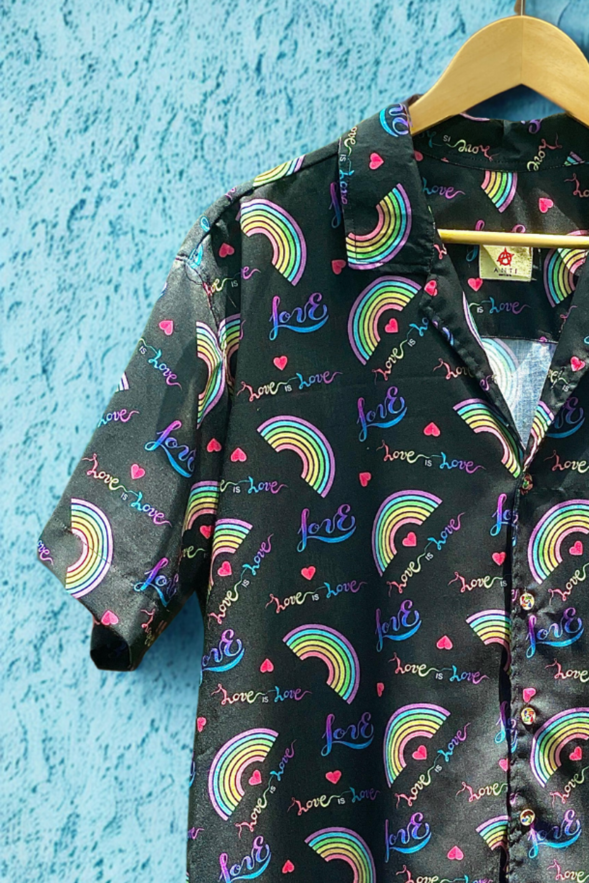 Close-up of chest and collar on ANTI’s cotton rainbow Pride shirt, featuring rainbow arcs, bold hearts, and empowering “love is love” graphics—designed for queer joy, trans pride, and fluid self-expression.