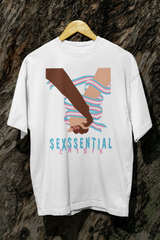 White gender-fluid t-shirt hanging against a textured tree bark background, featuring two hands—one dark-skinned, one light-skinned—grasped in solidarity and wrapped in the trans pride flag. Bold text below reads “SEXSSENTIAL CRISIS” in glitch-style fonts.

