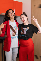 Two gender-diverse people smiling and posing in a kitchen, wearing ANTI’s “SEXXSENTIAL CRISIS” statement tees—featuring two interlocked hands wrapped in trans pride-colored ribbons. The graphic symbolizes queer solidarity, love, and empowerment through gender expression.

