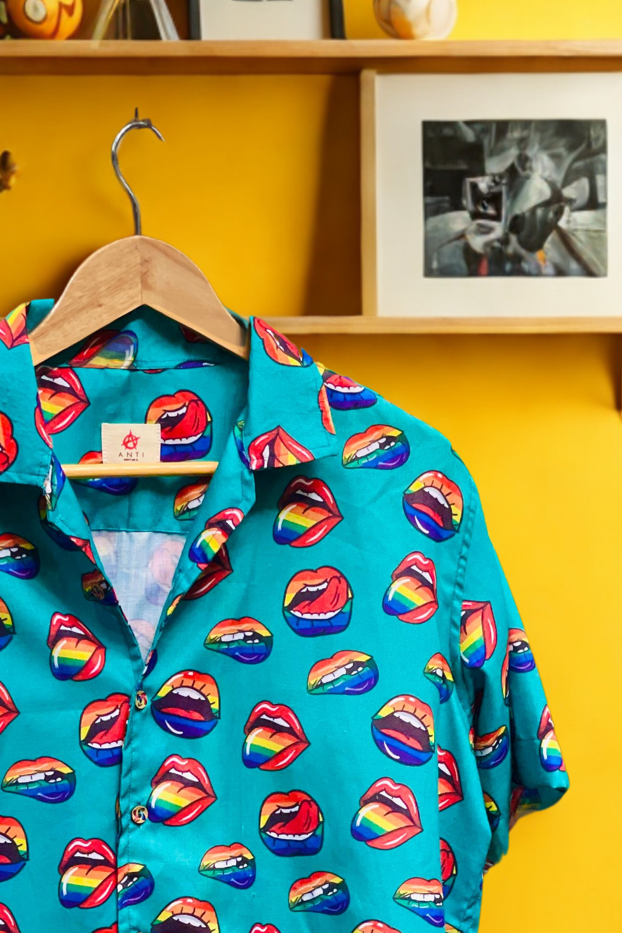Flat-lay of a black short-sleeve camp-collar shirt by ANTI, designed with repeated red open-mouth graphics printed throughout. The bold lips motif on dark fabric creates a striking contrast, combining punk attitude with queer symbolism. The relaxed fit and breathable fabric make this unisex shirt ideal for all-gender styling, queer streetwear looks, and expressive fashion statements during Pride or year-round.