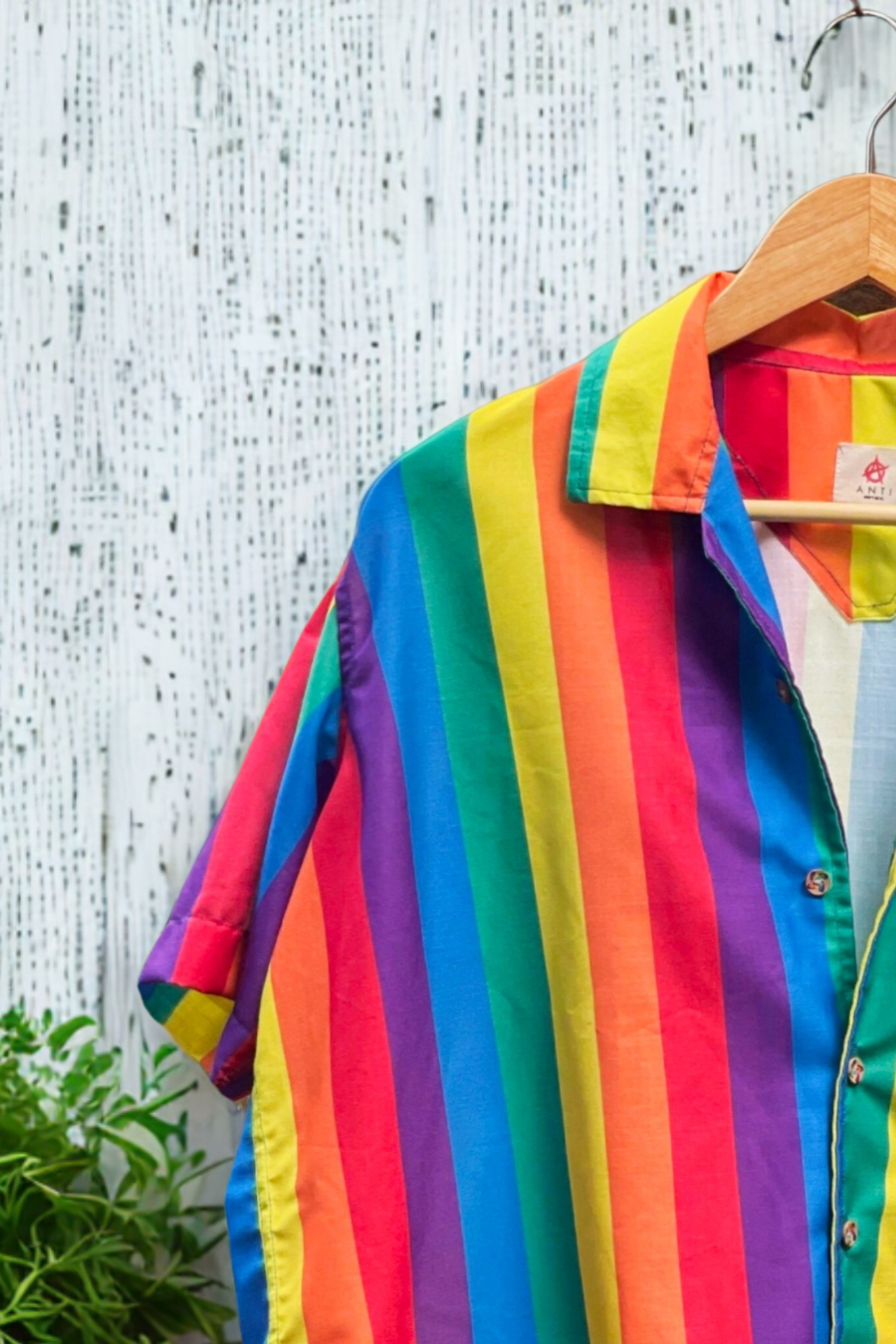 Close-up of rainbow-striped shirt with detailed ANTI brand label, emphasizing queer fashion, slow fashion, and identity-forward clothing.