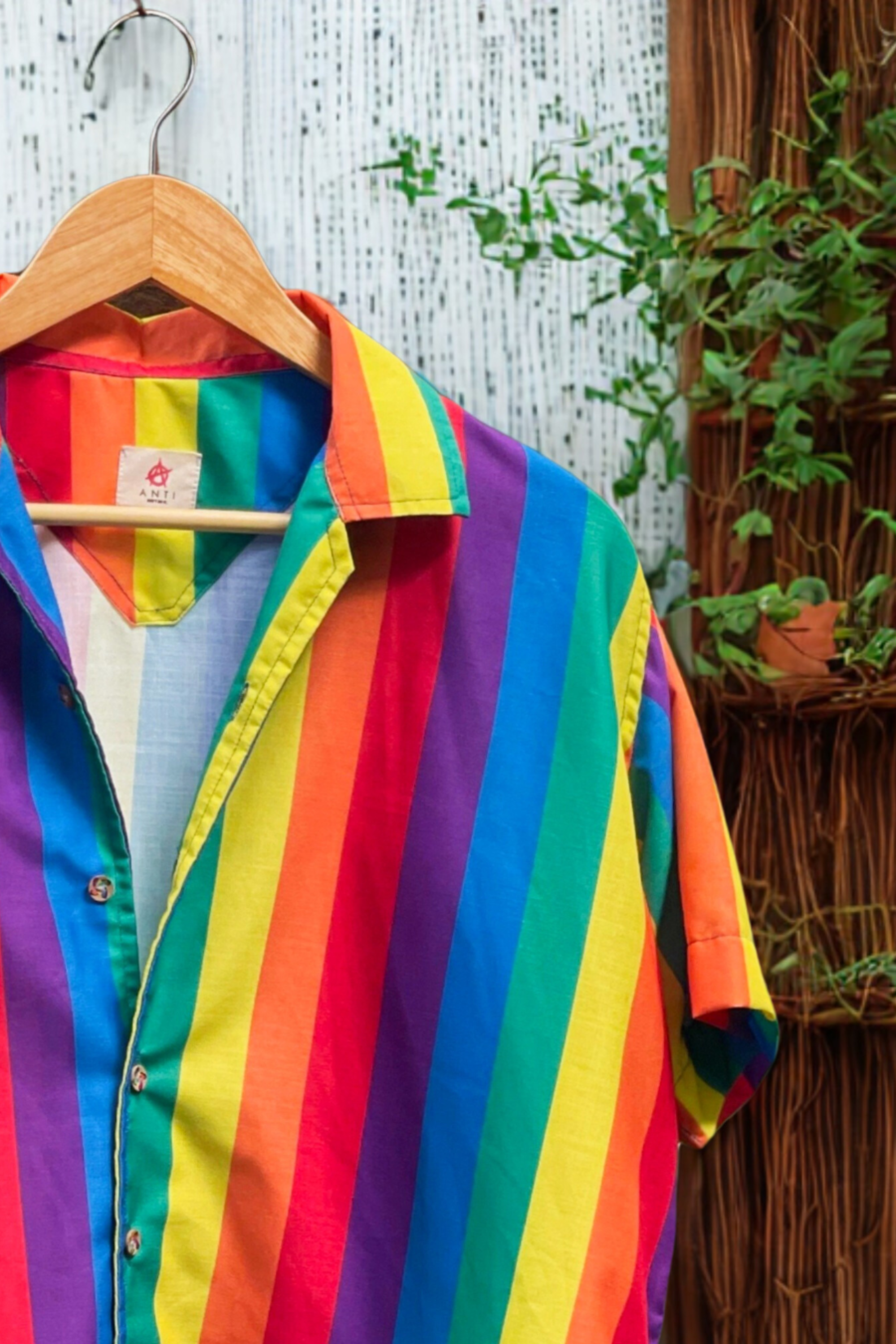 Close-up of rainbow-striped shirt with detailed ANTI brand label, emphasizing queer fashion, slow fashion, and identity-forward clothing.