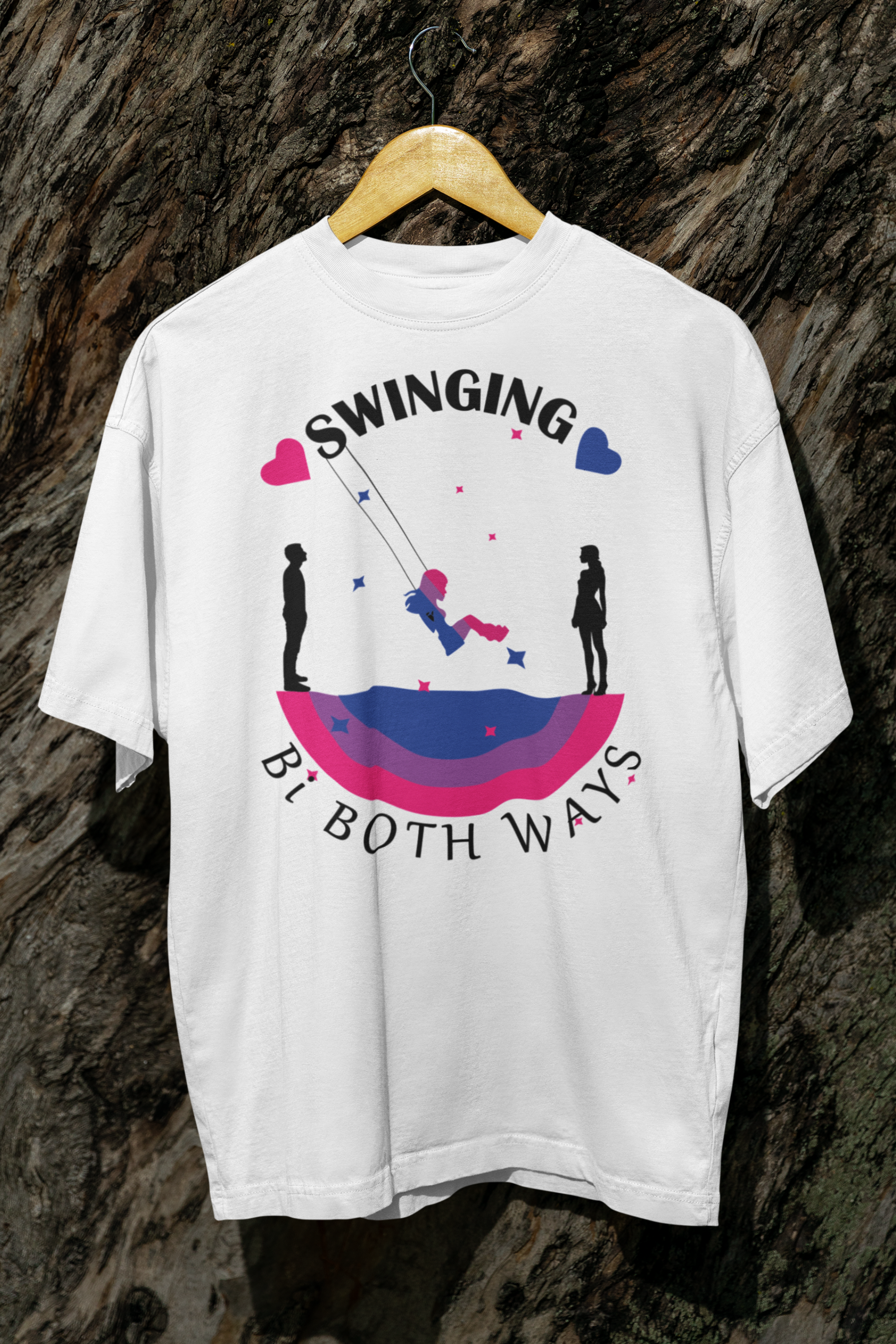 White bisexual pride graphic T-shirt displayed on a wooden hanger in front of tree bark. Design includes a swing silhouette and bi flag color arc beneath the phrase “Swinging Bi Both Ways,” symbolizing romantic fluidity with bold, inclusive flair.

