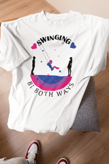 White unisex T-shirt laid on a chair, featuring a bold graphic of a person swinging between two silhouettes, framed by bi pride colors and the phrase “Swinging Bi Both Ways.” Playful and empowering design celebrates bisexual identity and fluidity in a gender-neutral cut.

