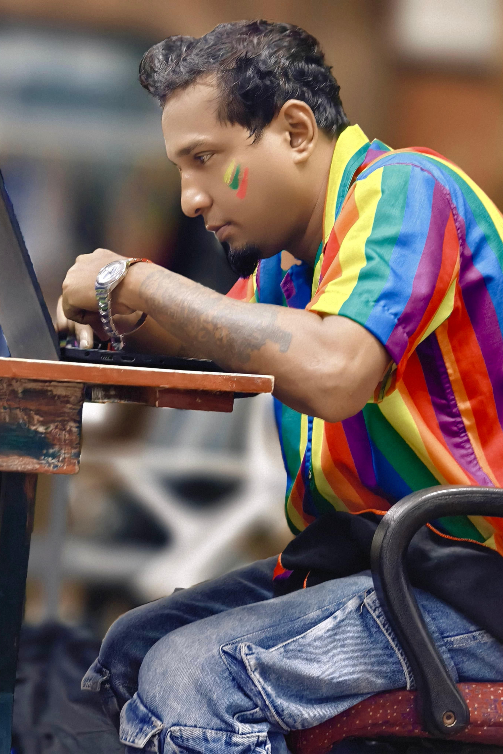 Person in rainbow ANTI shirt, seated while working with rainbow face paint — blending professional life with bold queer identity and pride.