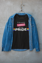 Black unisex t-shirt with the bold statement “In the world of LABELS, let's wear PRIDE” hanging on a hanger under a denim jacket against a minimalist concrete wall – a gender-neutral fashion statement by ANTI.